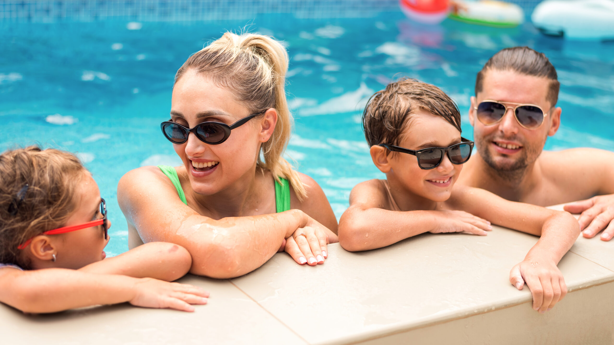 Happy parents and two kids are holding on to the side of the pool
